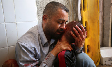 A man with bloodied hands cries while holding the head of an adolescent boy up to his face