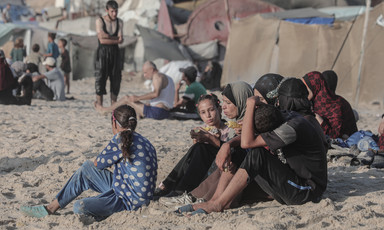A family sit beside tents on a beach 