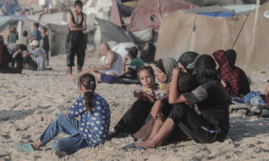 A family sit beside tents on a beach 
