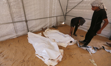 Two men stand beside a number of dead bodies wrapped in white shrouds 