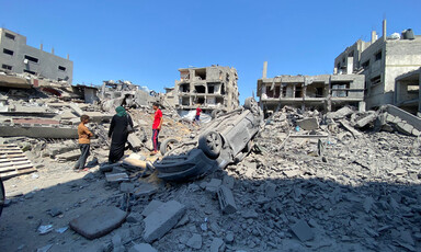 People beside an upturned car and rubble and the remains of buildings in Gaza 