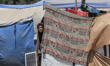 A woman peers out from behind a piece of cloth on a makeshift tent