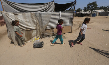 Displaced children walk beside a makeshift tent in Gaza 