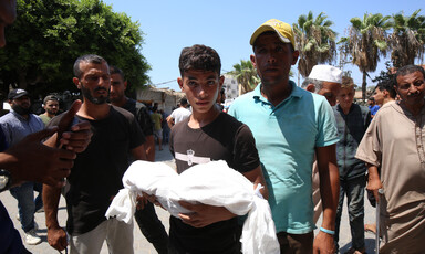 A young man carries a dead body wrapped in a white shroud