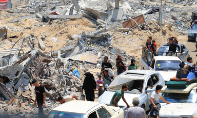 Heaps of rubble beside people walking and cars in southern Gaza 