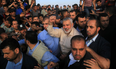 Ismail Haniyeh smiles and raises a fist in the middle of a crowd of men