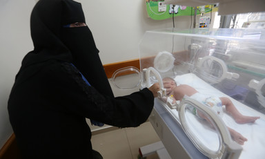A woman reaches for a baby in a NICU