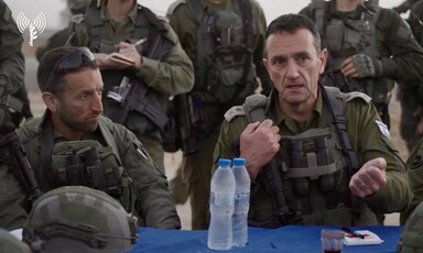 Hiram and Halevi in fatigues seated at table surrounded by armed soldiers