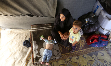 A woman sits on a rug on the ground with two little children