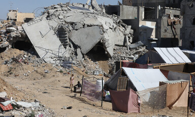 A homemade tent stands next to a destroyed building