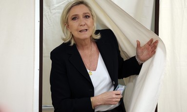 Marine Le Pen pushing a curtain away and holding a mobile phone in her other hand 