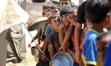 Palestinian boys, some holding pots, stand in a line at a food distribution site.