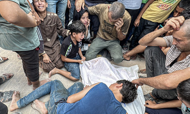 Men and children encircle and mourn a body covered in a white cloth.