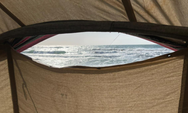 A slit from a white tent looks out onto a sliver of ocean view