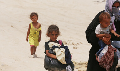 A woman holds a baby while two other children walk beside or behind her 
