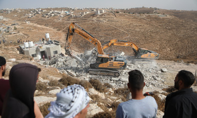 People watch two bulldozers destroy a house