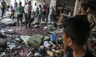 People stand around a room filled with ashen and blood-stained personal belongings