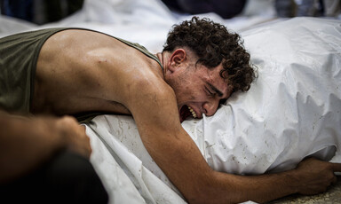 Close-up of a young man with an anguished face embracing a shrouded body 