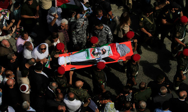 Aerial view of body wrapped in Palestine flag carried on stretcher in crowd