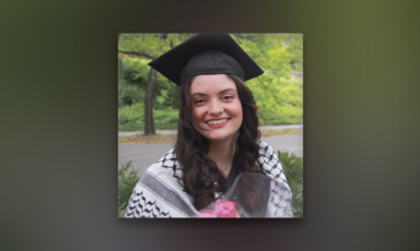 Young woman wearing graduation cap and a kuffiyeh around her shoulders smiles while looking toward camera