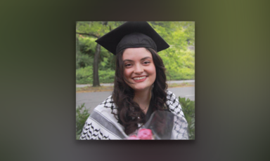 Young woman wearing graduation cap and a kuffiyeh around her shoulders smiles while looking toward camera