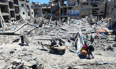 Young men push a bicycle and ride a donkey-drawn cart carrying their possessions along a bombed-out road
