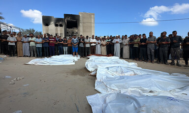 People pray over a row of shrouded corpses