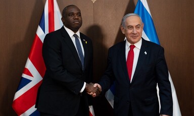 Two men in suits shaking hands in front of the British and Israeli flags