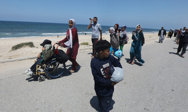 People wsalking along a sandy road carrying their belongings