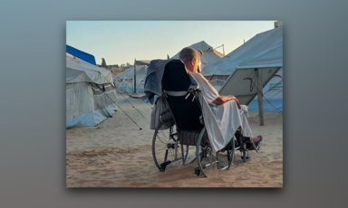 With his back to the camera, a man sits in his wheelchair amid tents in the sand