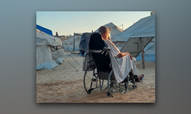 With his back to the camera, a man sits in his wheelchair amid tents in the sand