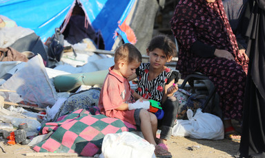 Two children sit in front of a tent that has become their shelter