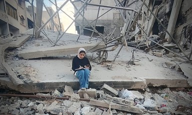 A woman sits studying in rubble