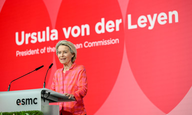 European Commission President Urusla von der Leyen stands at a podium with her name written behind her in white on a red backdrop