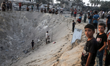 Boys look at camera as people stand on edge of sandy crater