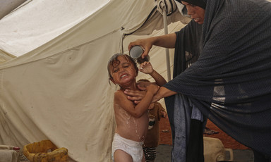 A woman bathes her child with a cup of water