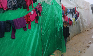 A young girl stands next to plastic sheeted tents with clothes hanging on lines
