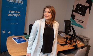 Woman stands in front of a desk with a blue backdrop reading Renaissance 