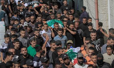 A large crowd carries corpses on stretchers wrapped in flags.