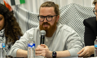 A man holds up and speaks into a microphone sitting between two people