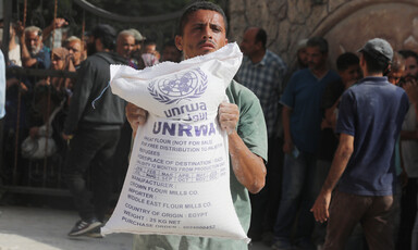A man holds a large bag of flour bearing UNRWA's name and logo