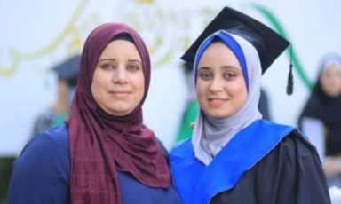 Two women, one in a graduation cap, smile for the camera.