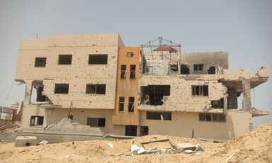 A daytime view of a building riddled with bullet holes and damage from explosives. 