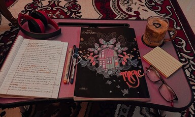 A writer's desk with a notebook, pens, paper and a cup of coffee.