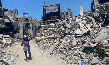 A boy wearing a pot as a helmet walks through rubble