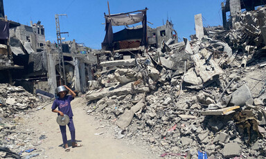 A boy wearing a pot as a helmet walks through rubble