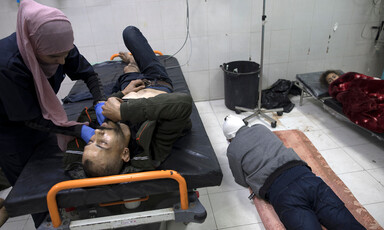 Two patients lie on the floor next to one occupied hospital bed