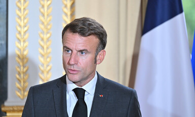 French President Emmanuel Macron stands with a flag behind him