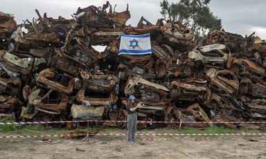 A woman takes a selfie in front of a stack of crushed cars and an Israeli flag