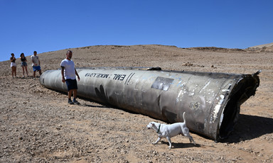 A man and a pet dog stand next to a massive missile fragment on a barren landscape